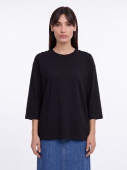 Bella לובשת חולצה שחורה בגזרה רחבה של TAL DEUTSCH עם חצאית ג׳ינס כחולה